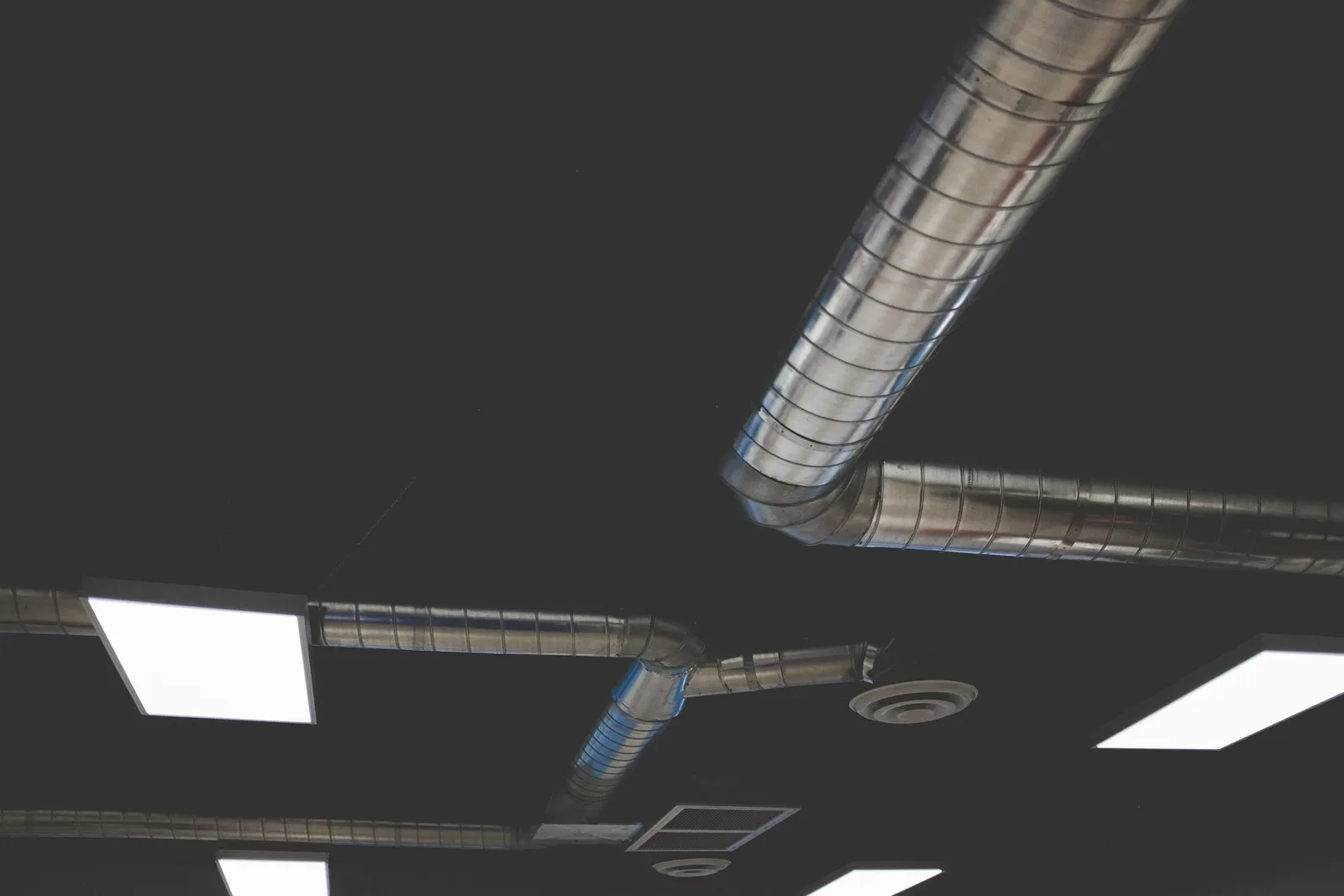Exposed spiral metal ductwork and a supply diffuser on a dark ceiling