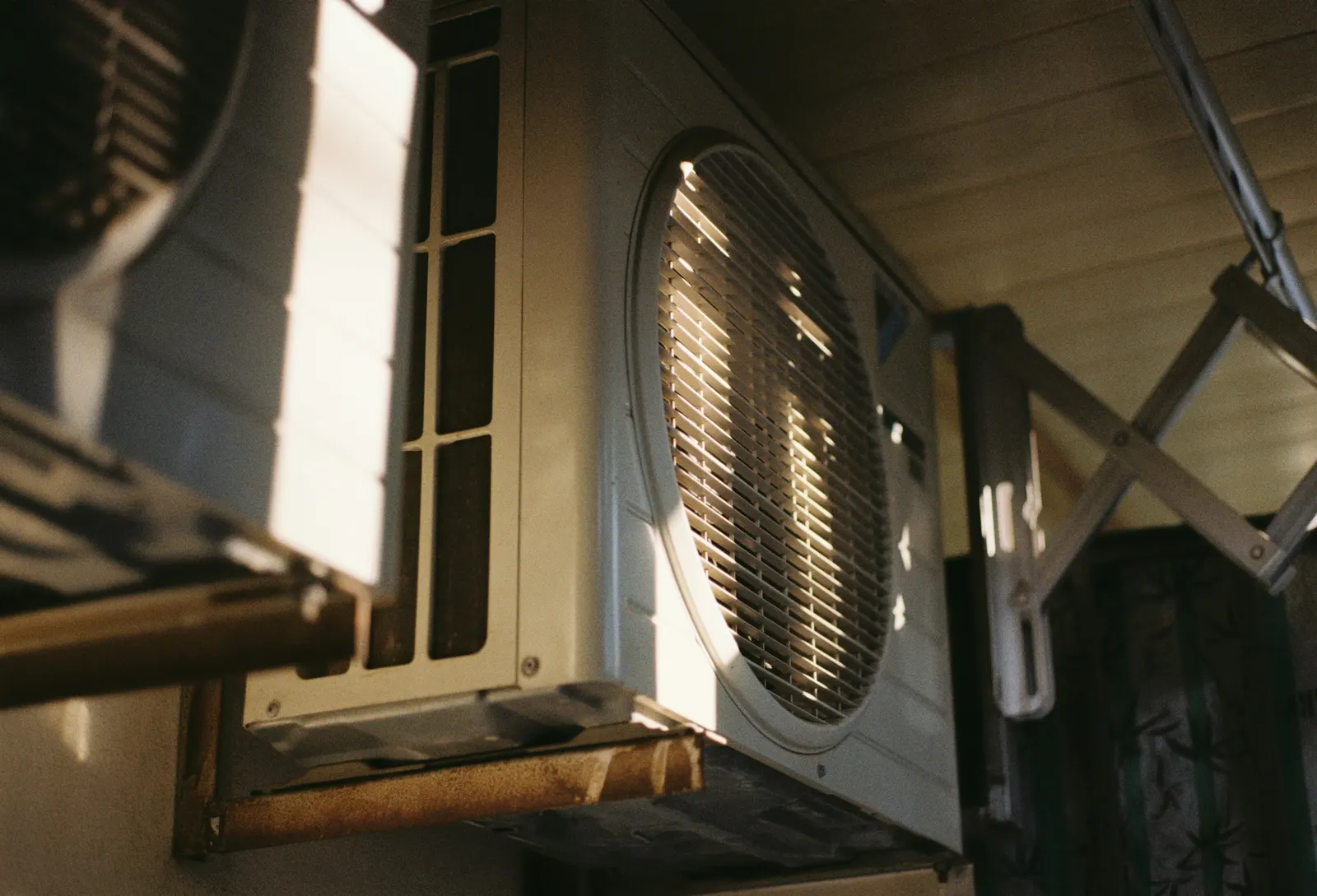 Outdoor air conditioner unit mounted under an eave in late sun