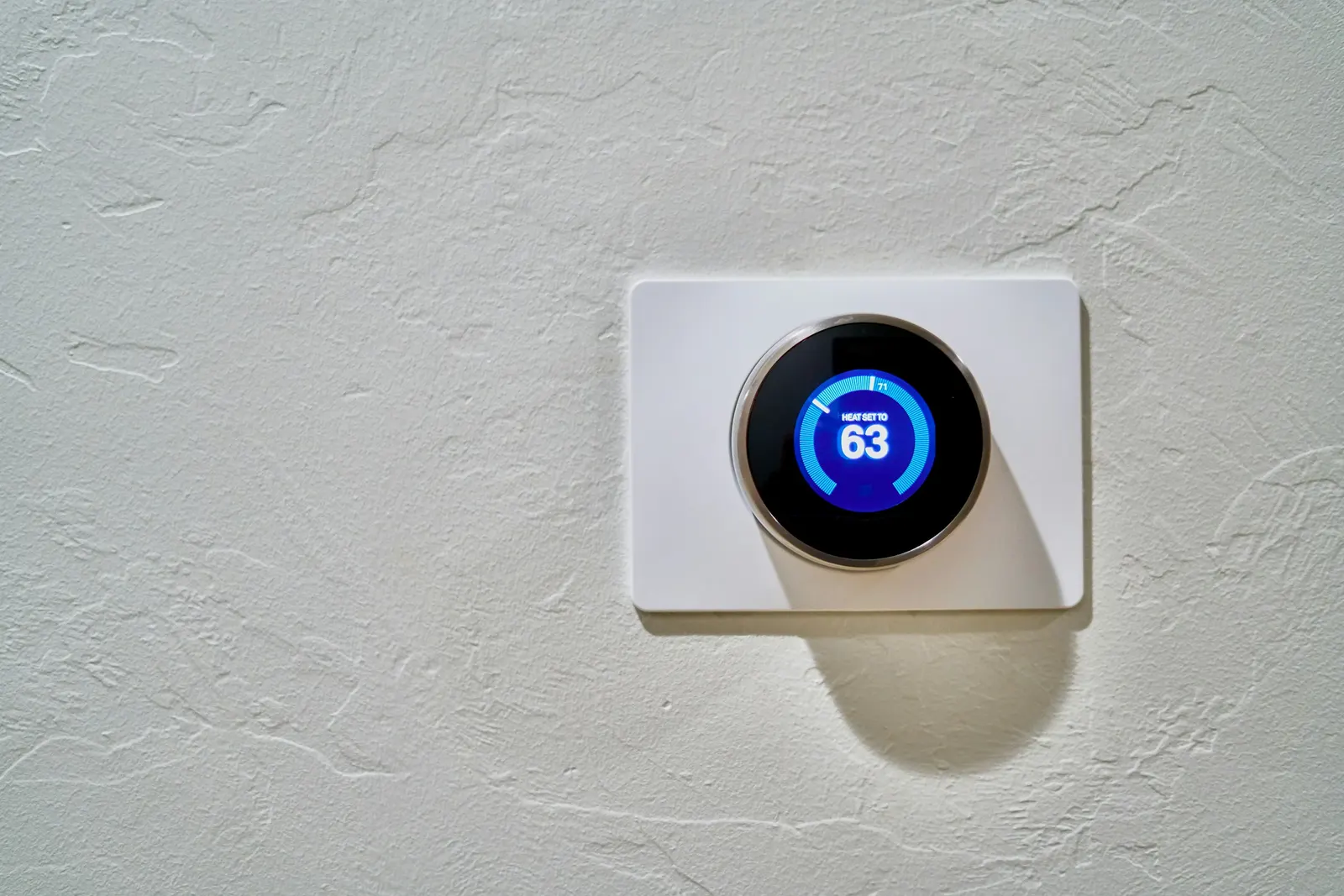 Smart thermostat on a textured wall showing a heat setting of 63