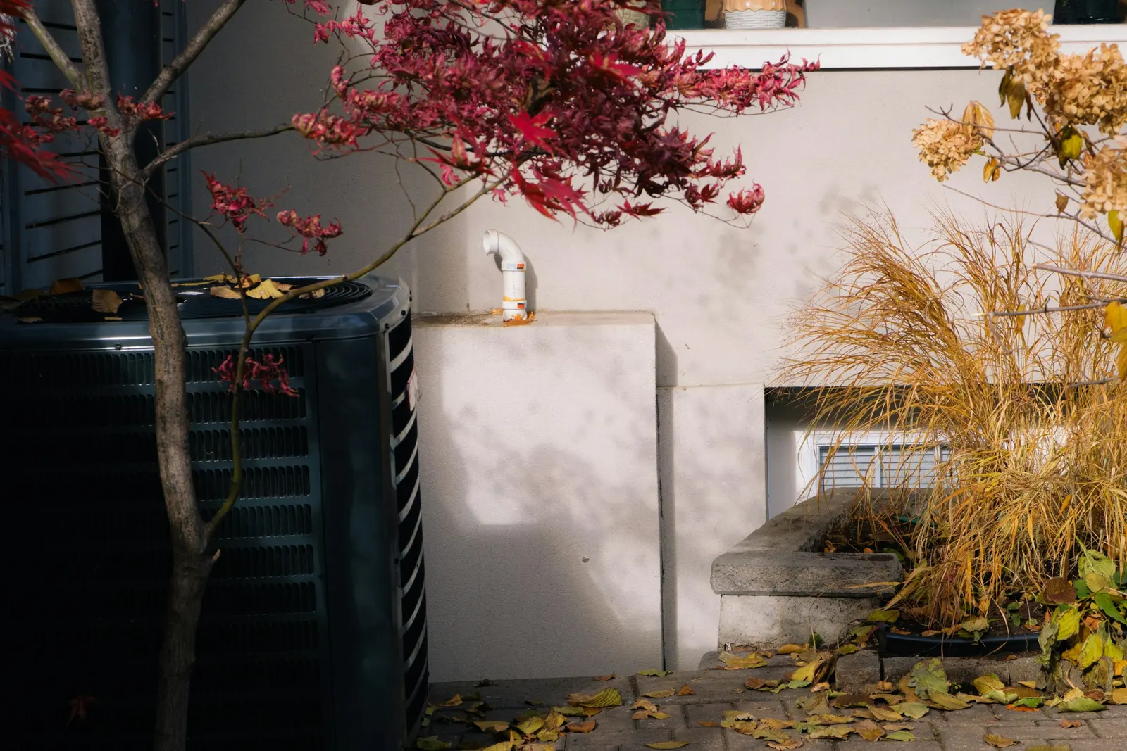 Outdoor condenser unit beside a house with autumn leaves