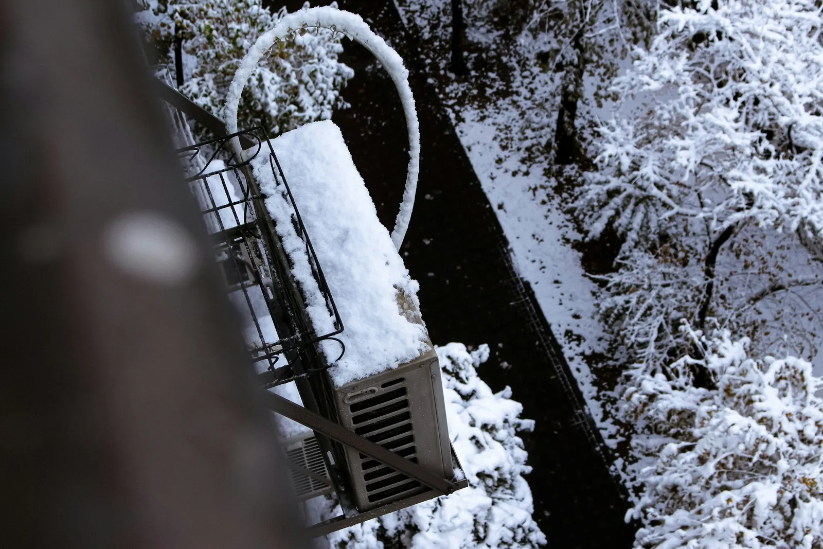 Snow-covered outdoor heating and cooling unit on a balcony bracket
