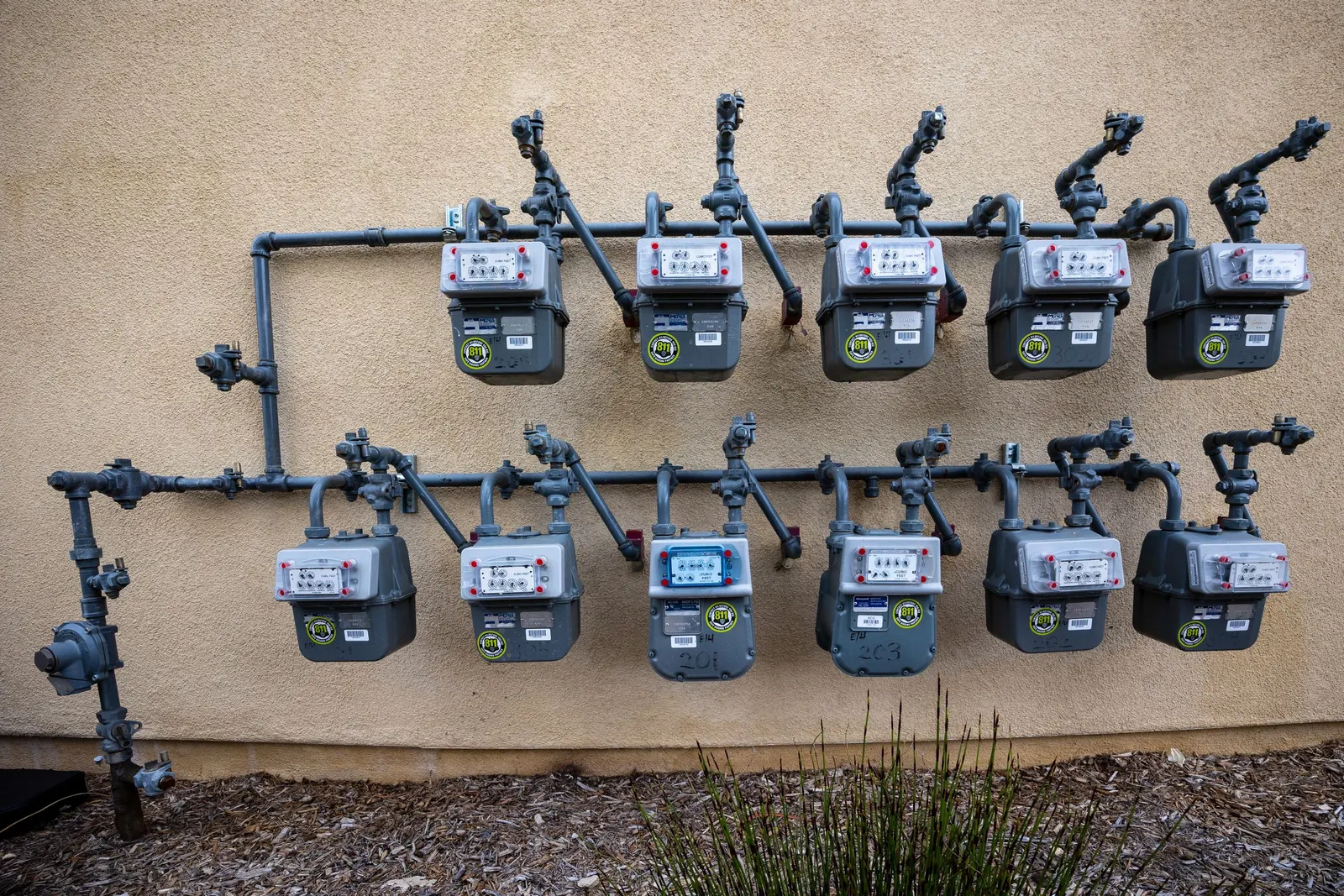 Two rows of residential gas meters on a stucco wall
