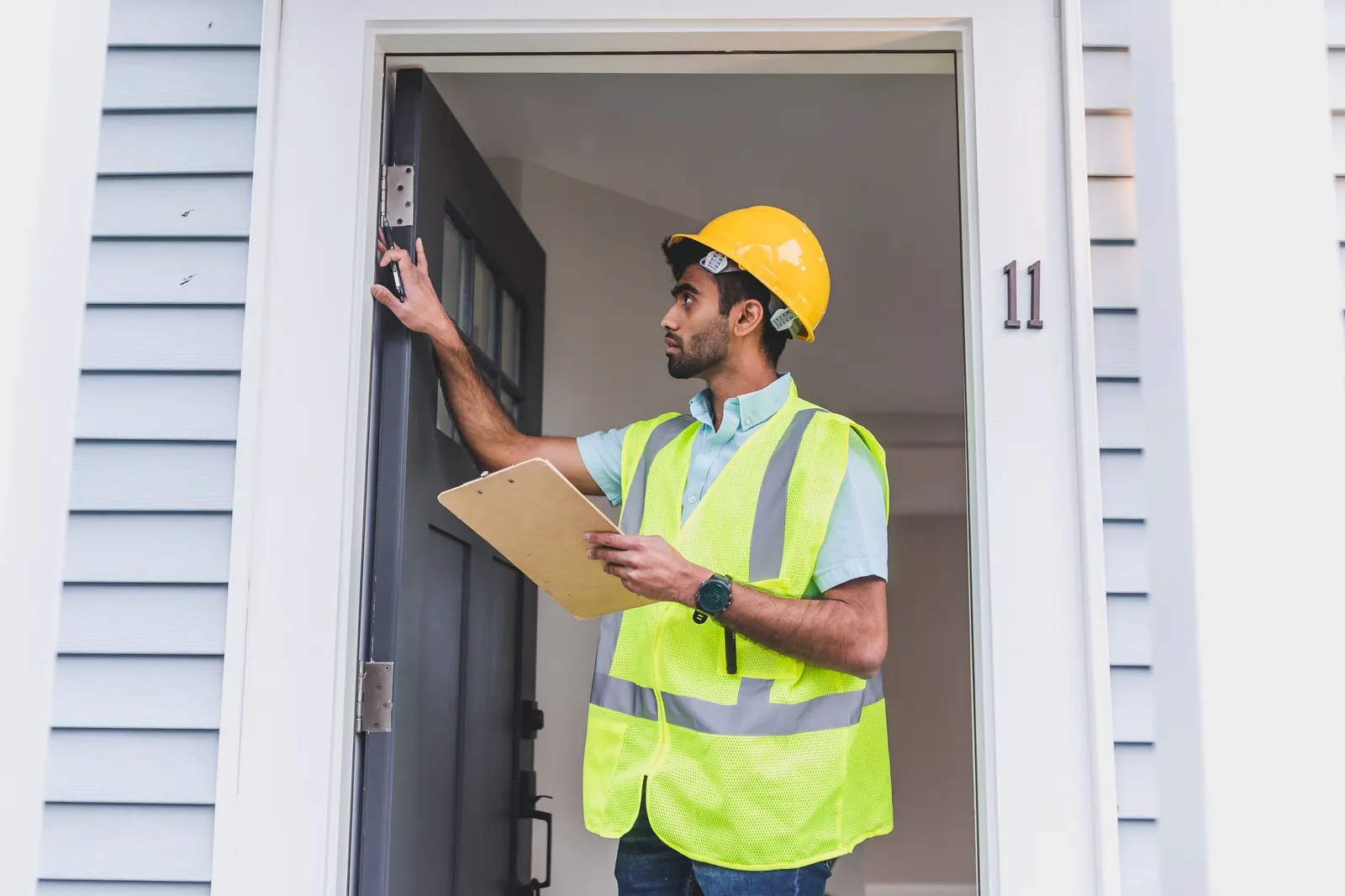 Inspector in a hard hat and safety vest checking a doorframe with a clipboard