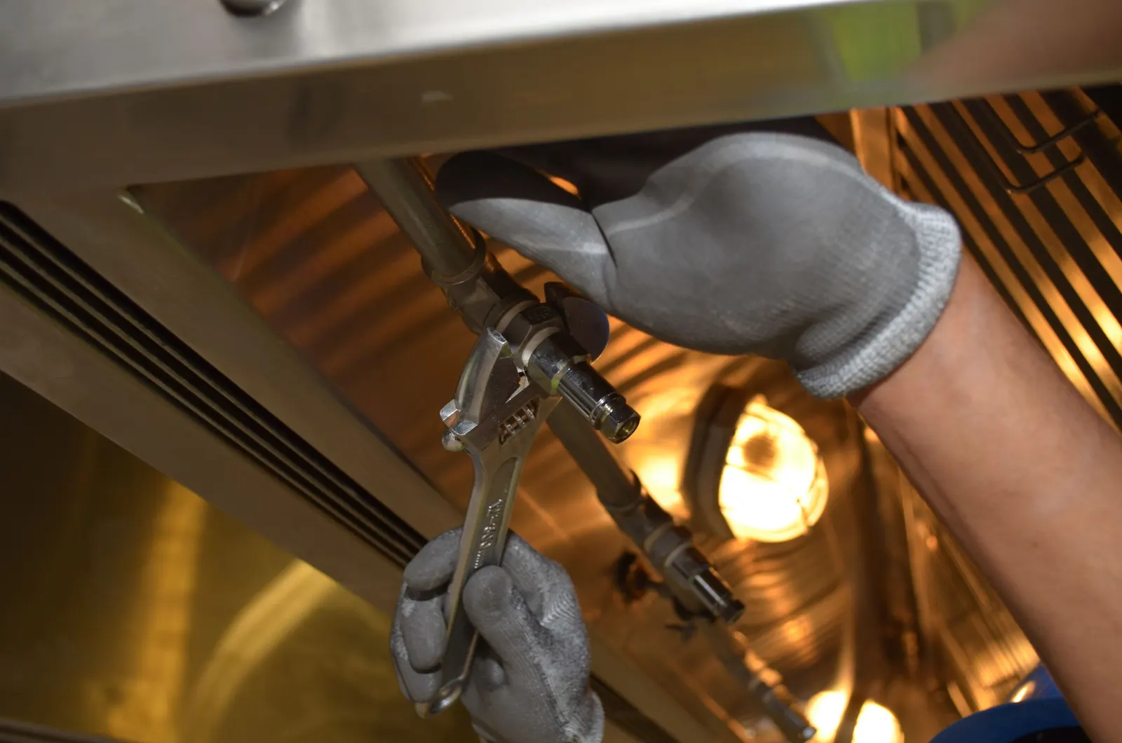 Gloved hands tightening a pipe fitting with an adjustable wrench