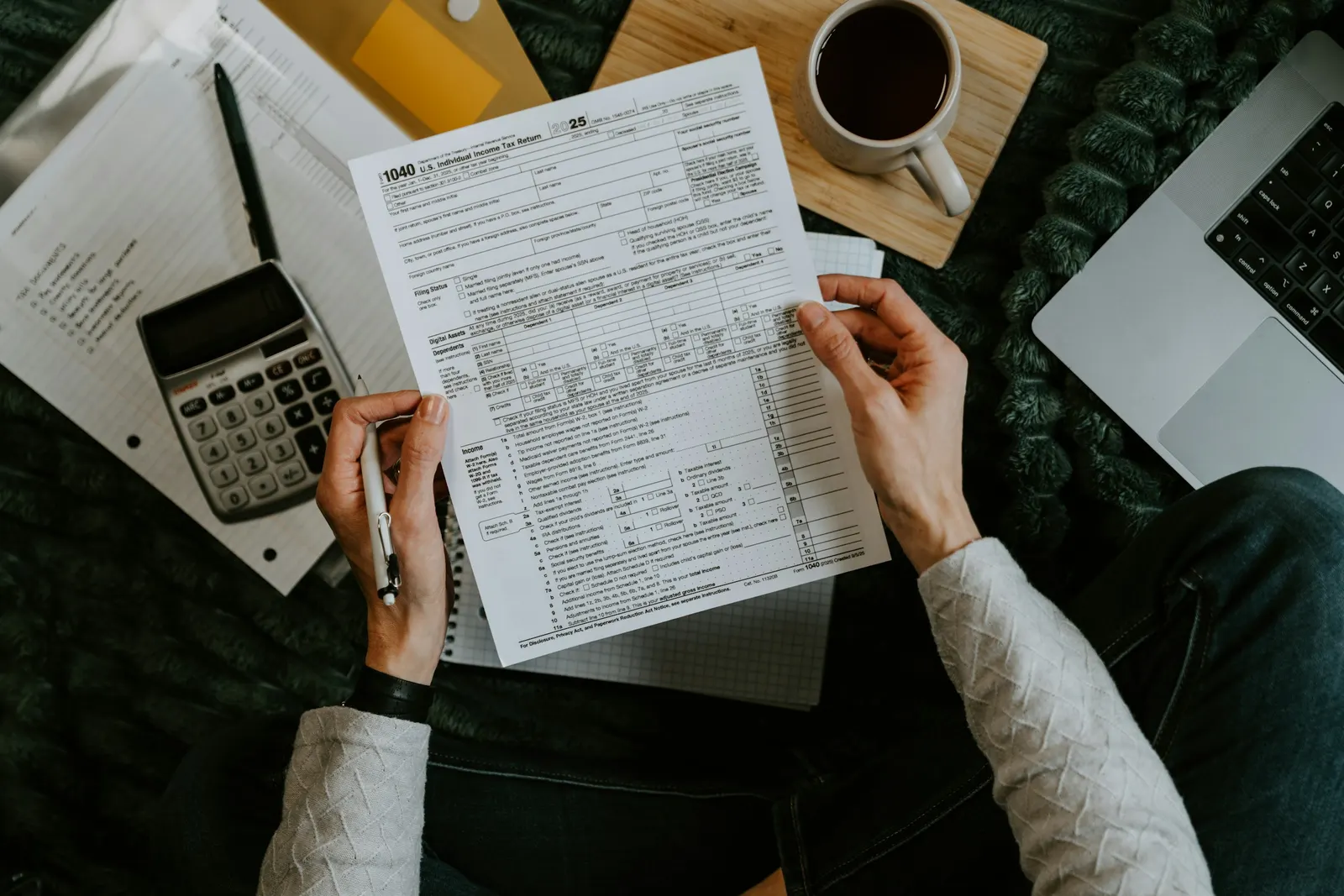 Hands holding a federal Form 1040 beside a calculator and laptop.