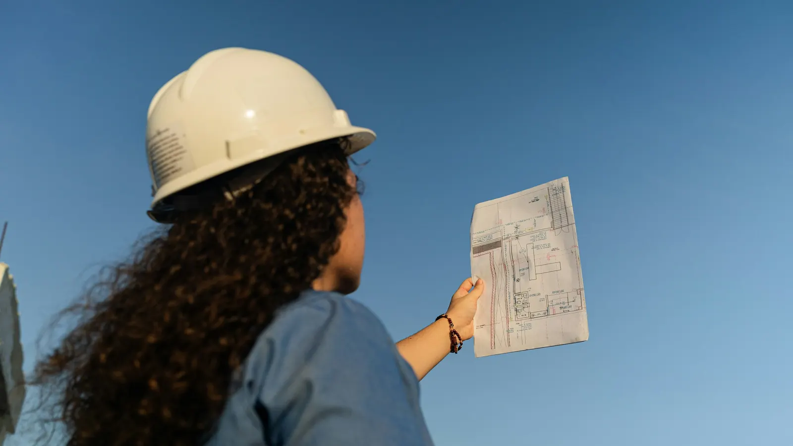 A worker in a hard hat holds up a building plan.